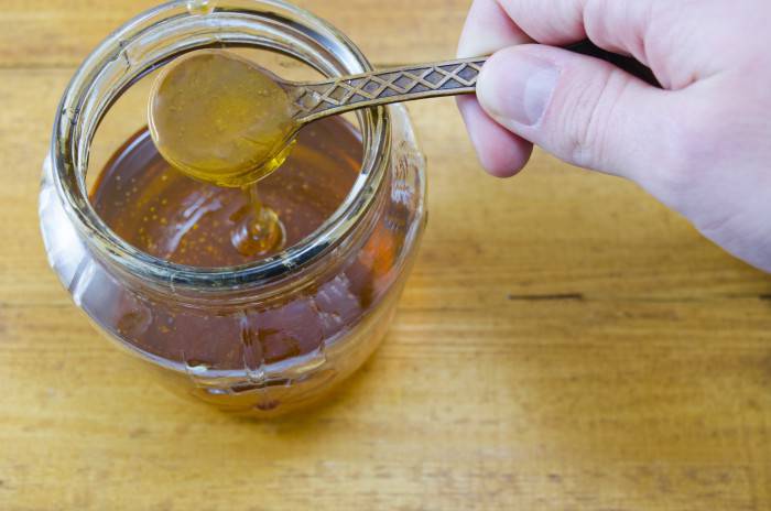 Hand holding a spoon of honey above the jar