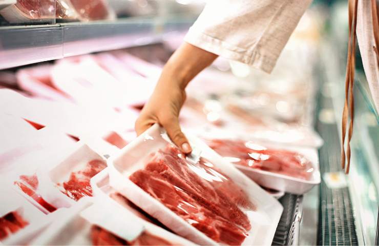 Una persona raccoglie della carne messa in vendita in un supermercato