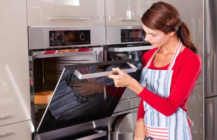 Una donna controlla la pietanza messa a cuocere in forno